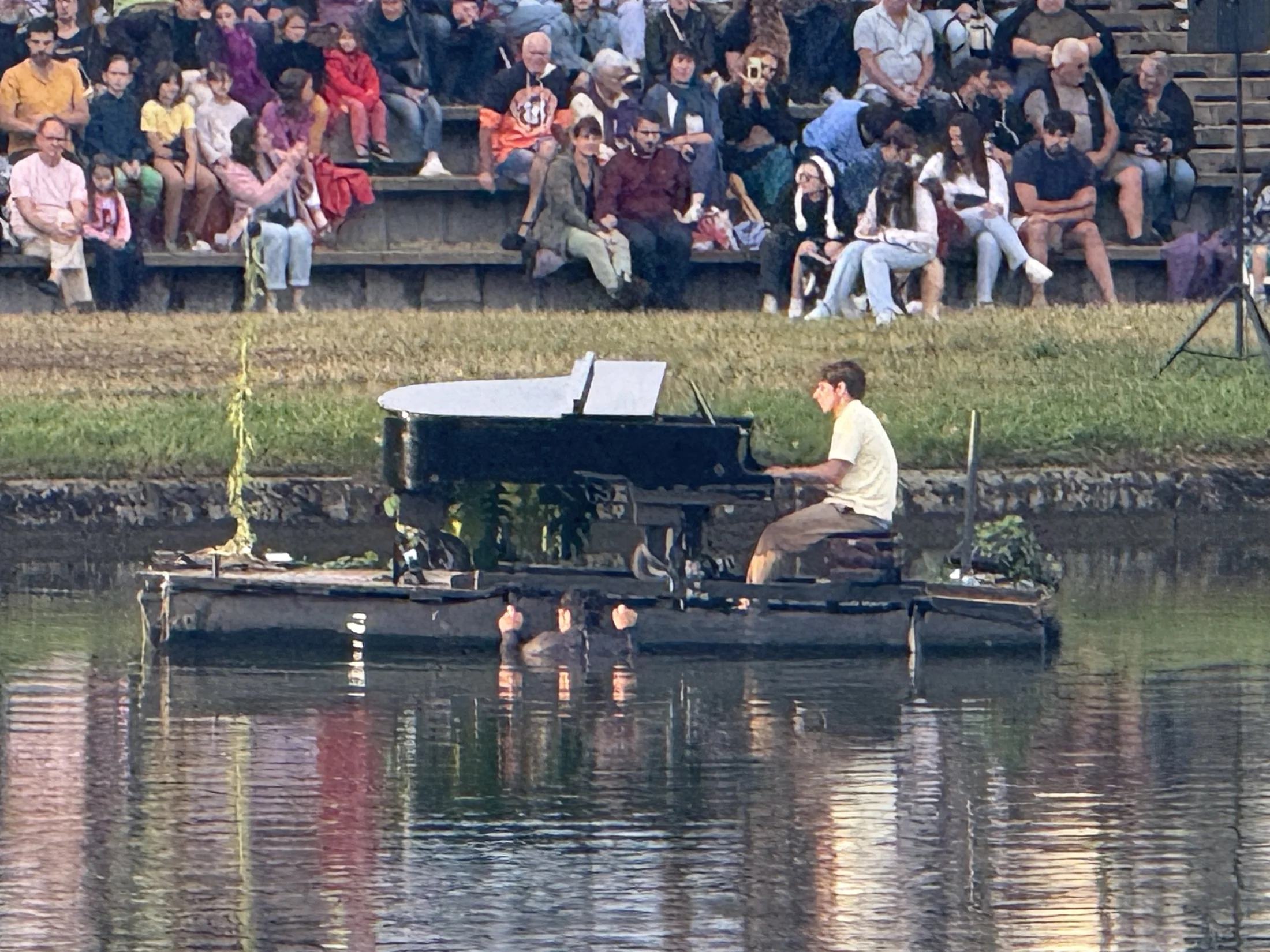 Een pianist bespeelt een vleugel op een drijvend podium in de havenkom van Génelard, met publiek op de oever