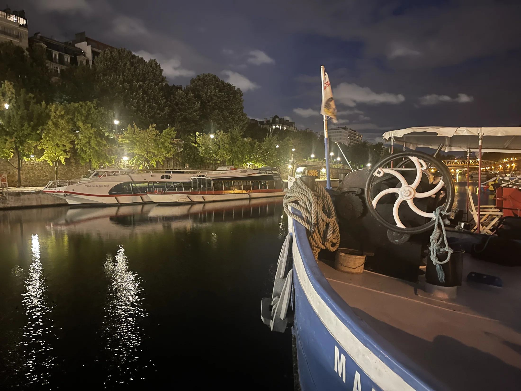 La proue de Maria la nuit, avec les bateaux amarrés et les lumières qui se reflètent dans le Port de l’Arsenal
