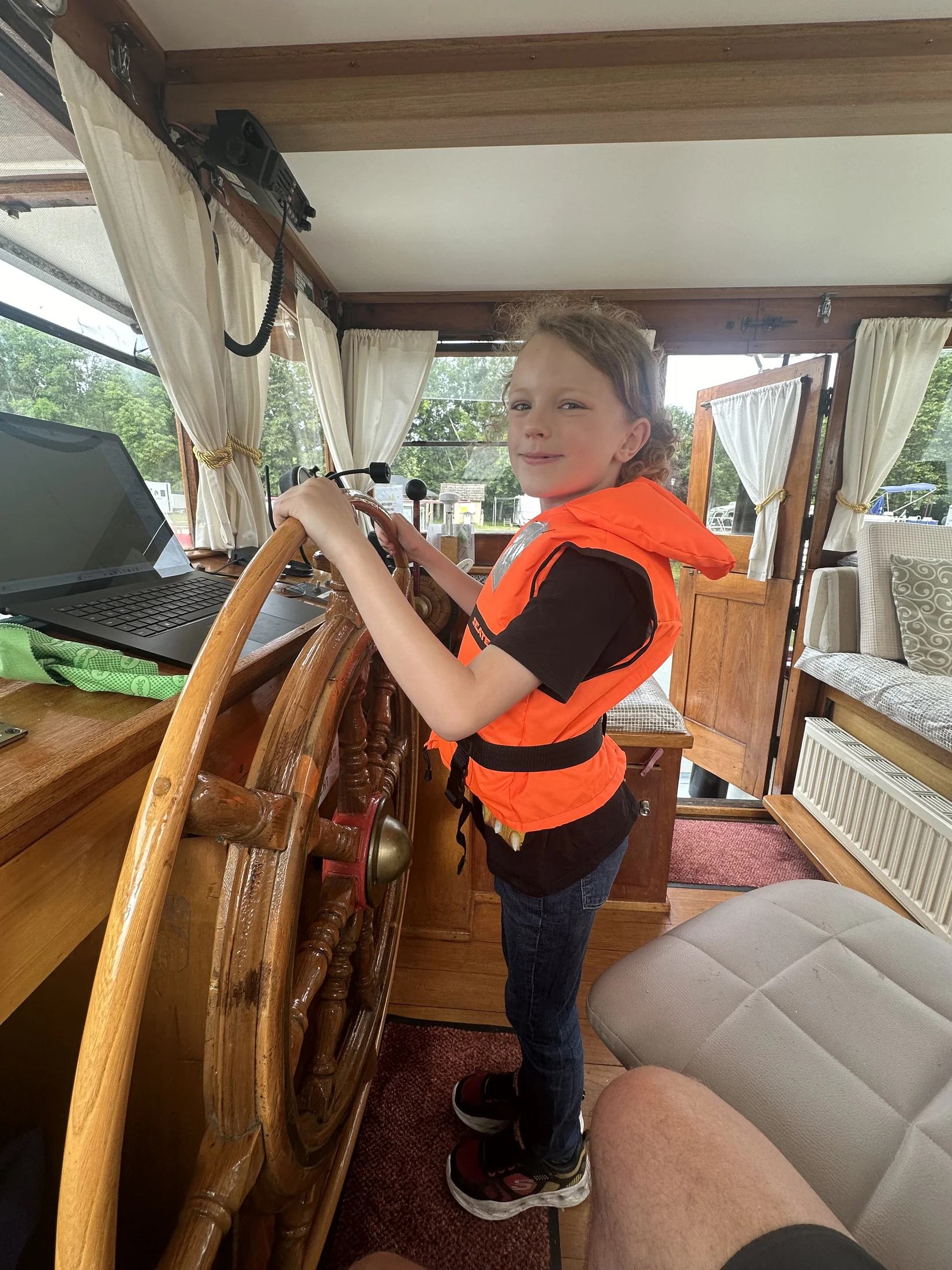 Harry draagt een reddingsvest en houdt Maria’s houten stuurwiel vast in de stuurhut