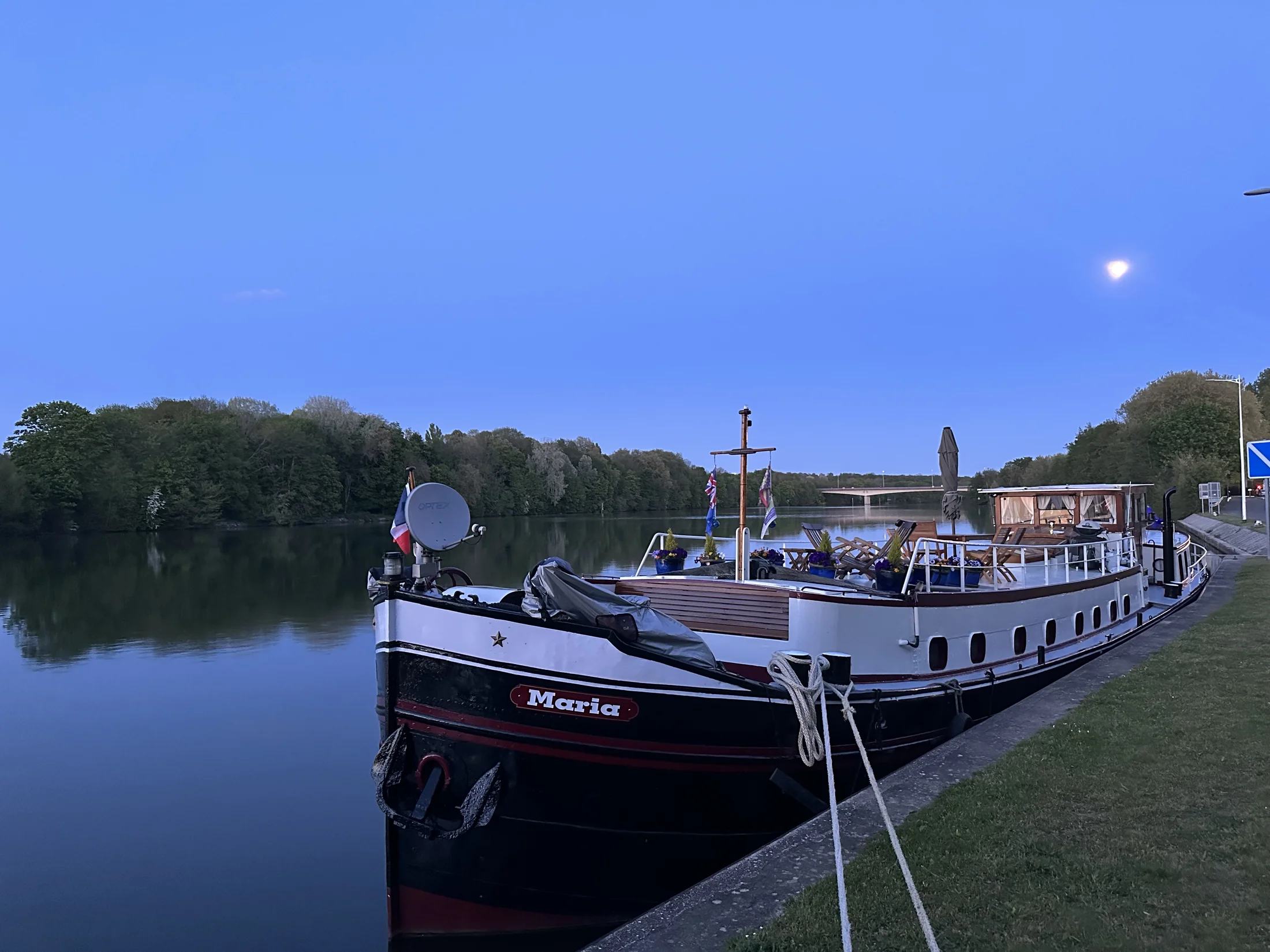 Maria afgemeerd naast een groene oever in het stille blauwe avondlicht