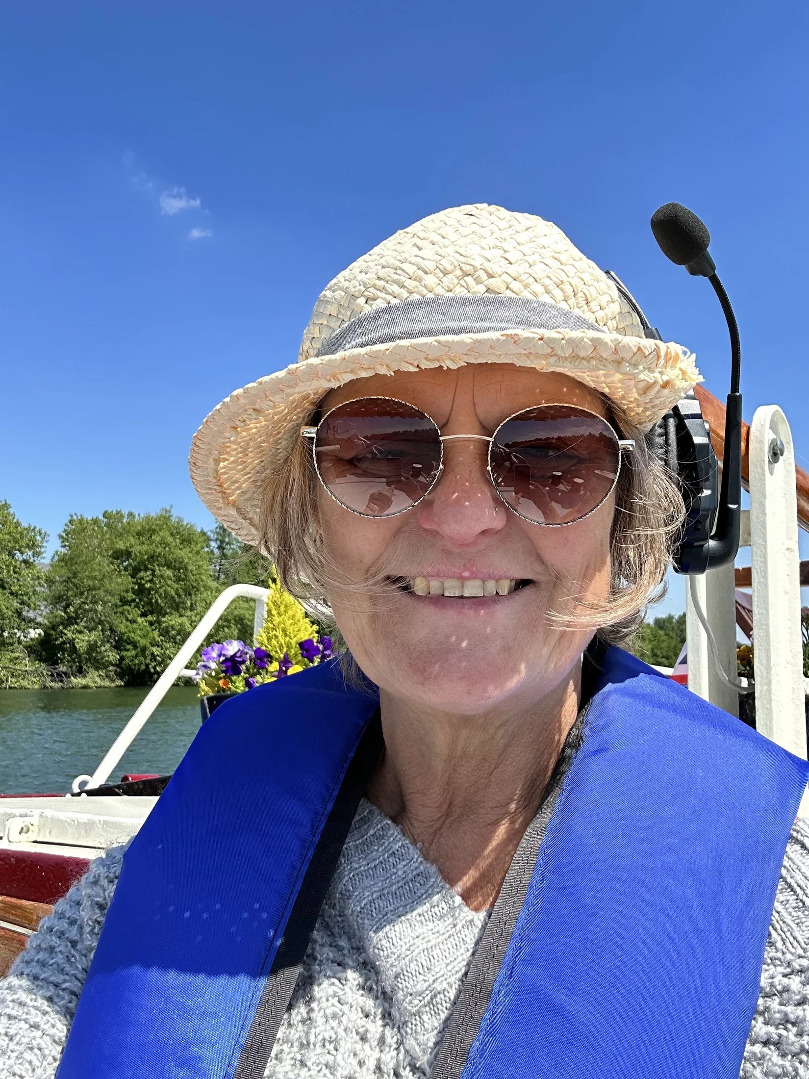 Kaz glimlacht aan boord van Maria, met een zonnehoed en reddingsvest