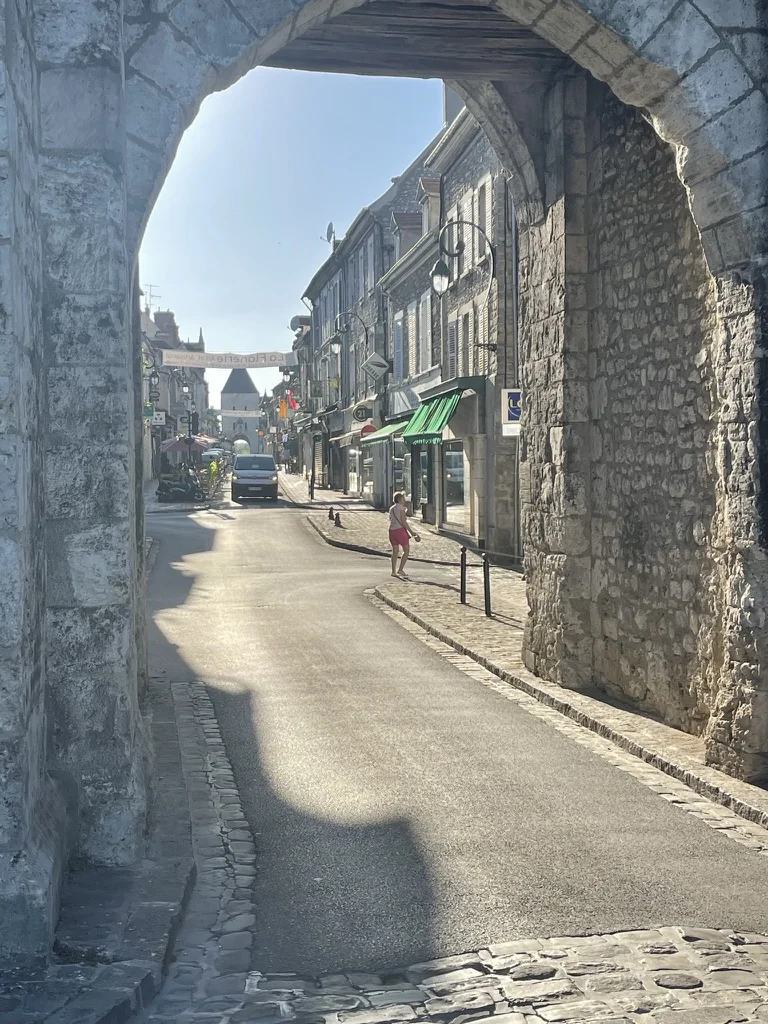 Une rue ensoleillée vue à travers une porte médiévale en pierre à Moret-sur-Loing