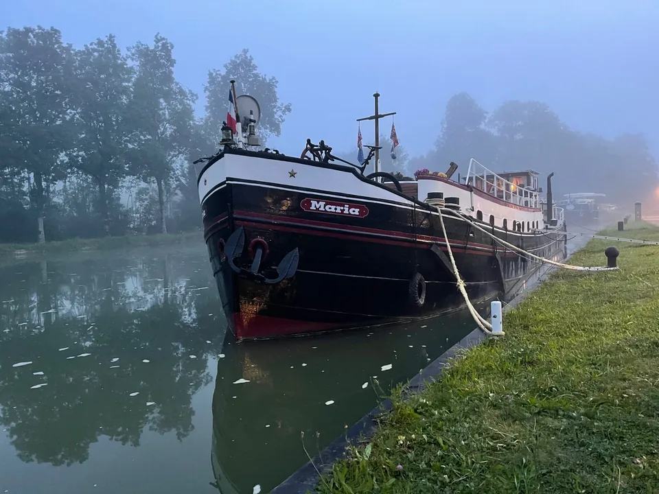 Maria amarrée sur une eau calme dans la brume du petit matin, sa proue et son nom bien visibles